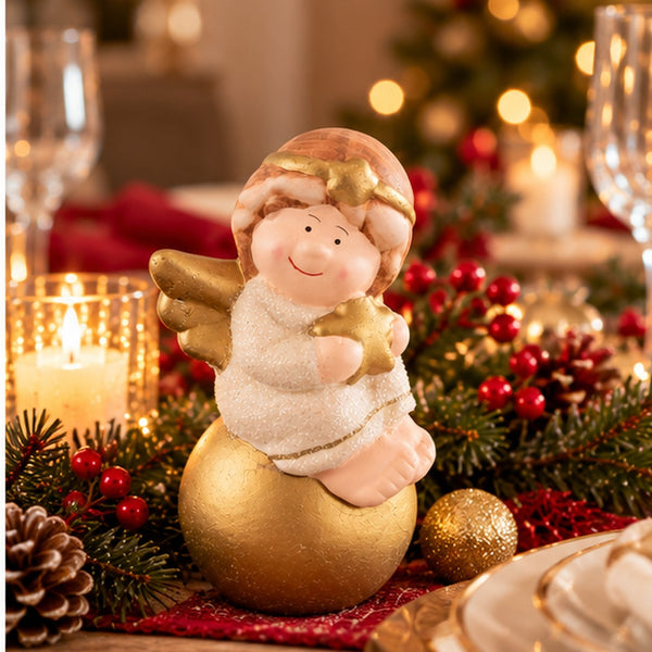A Christmas angel figurine sitting on a gold ornament, placed on a decorated holiday table with candles, pinecones, and red berries.