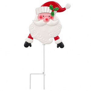 A festive Christmas yard sign shaped like a smiling Santa Claus head with a red hat, white beard, pink cheeks, green holly accent, and black gloves, mounted on a white metal stake against a plain white background.