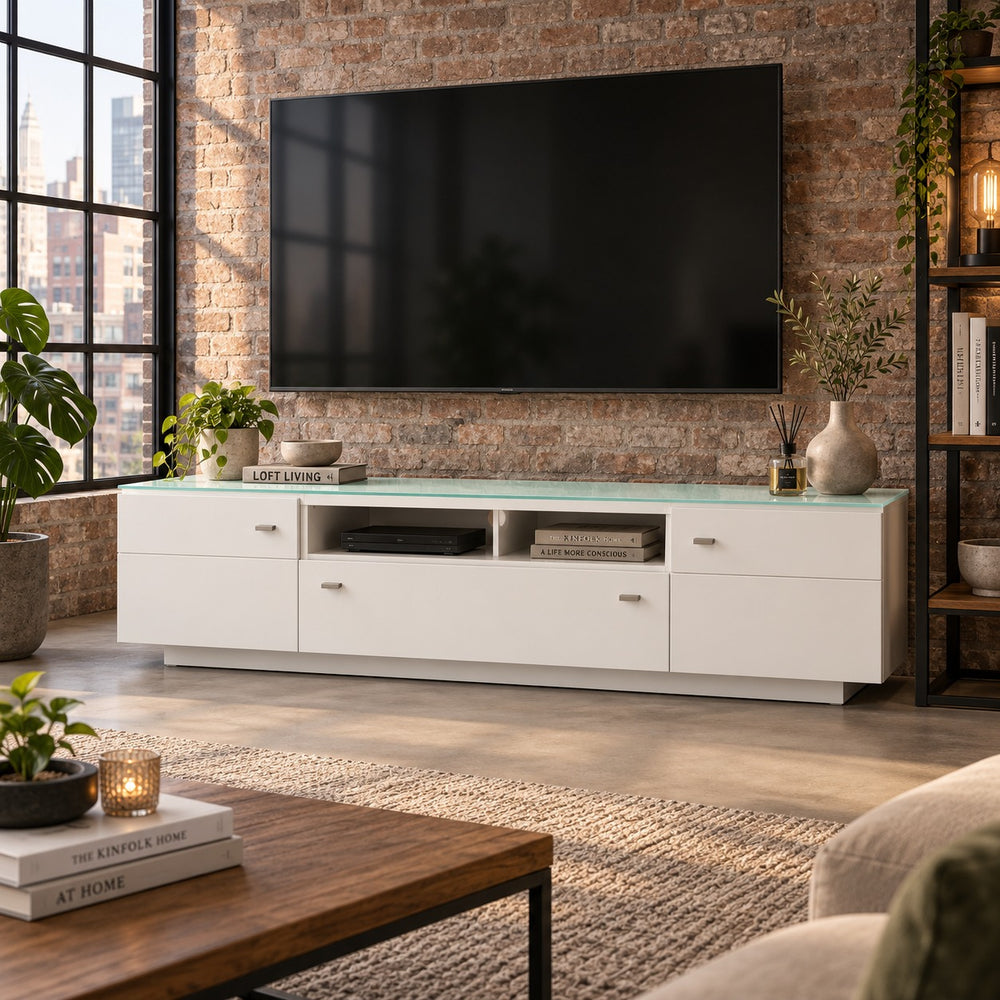 A modern white media console with a translucent mint green glass top, styled in a living room setting against a brick wall with a large black TV mounted above it.