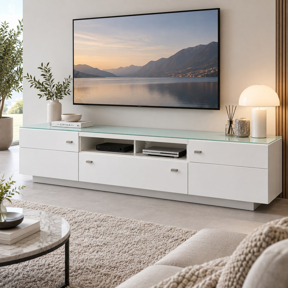A modern white media console with a translucent mint green glass top, styled in a living room setting against a brick wall with a large black TV mounted above it.