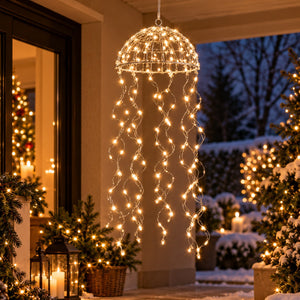 A hanging dome-shaped string light fixture with warm white LED lights draped downward, displayed on a snowy porch at dusk with outdoor holiday decorations in the background.