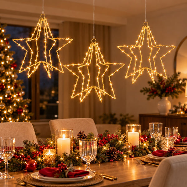 Three glowing star-shaped Christmas light decorations hang above a warmly lit dining table set with candles, plates, and holiday greenery in a cozy indoor holiday setting.