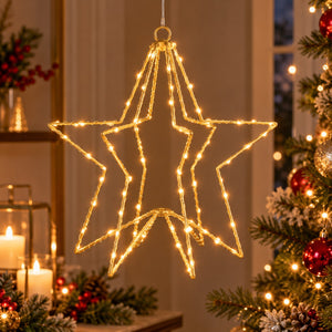 A large five-pointed star-shaped light fixture with warm white LED lights, hanging in a decorated Christmas setting with a lit tree and candles in the background.