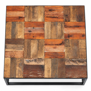A square coffee table with a rustic patchwork top made of reclaimed wooden planks in various shades of brown, orange, and beige, supported by a black metal frame.