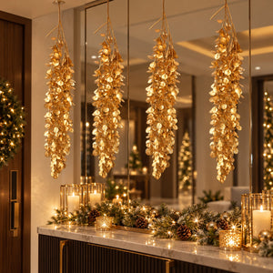 Three hanging gold leaf garlands with warm white string lights are displayed in a luxurious entryway with large mirrors, a marble console table, and festive holiday decorations.