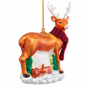 A Christmas ornament shaped like a deer standing on a snowy base. The deer has white antlers, an orange-brown body, a red and black checkered scarf, green textured patches near its legs, and a gold hanging string above it.