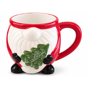 A ceramic mug shaped like a gnome's face, featuring a white body with a red rim and handle, black feet, and a green holly leaf detail on the front, set against a plain white background.