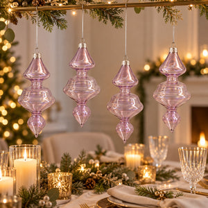 Four lavender purple ribbed glass Christmas tree ornaments hanging from a gold garland over a beautifully set dining table with candles and greenery.