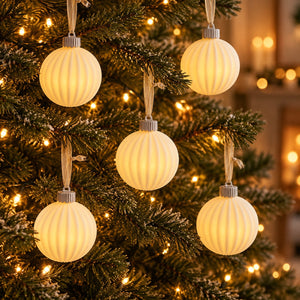 Five ribbed cream-colored spherical Christmas tree ornaments with silver caps and hanging ribbons, shown lit and hanging on a decorated Christmas tree with warm lights.