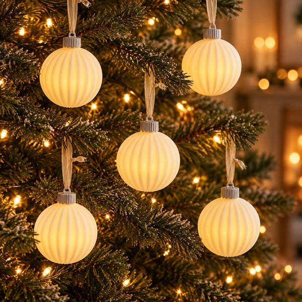 Five ribbed cream-colored spherical Christmas tree ornaments with silver caps and hanging ribbons, shown lit and hanging on a decorated Christmas tree with warm lights.