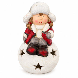 A small decorative figurine of a child in winter clothing sitting on a snowball base with star cutouts, photographed on a plain white background.