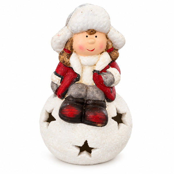 A small decorative figurine of a child in winter clothing sitting on a snowball base with star cutouts, photographed on a plain white background.