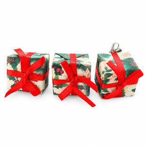 Three small Christmas ornament shaped like wrapped gift boxes, decorated with a green and cream holly pattern and tied with bright red ribbons, on a white background.