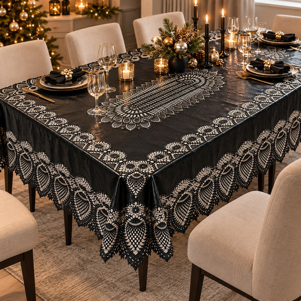 A black tablecloth with an intricate white embroidered or lace-like border and central floral pattern, draped over a dining table set with plates, wine glasses, candles, and holiday decorations in a warmly lit room.