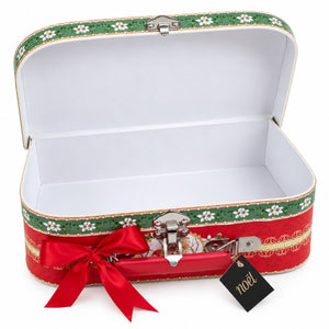 A decorative open suitcase-shaped box with a red exterior, green floral trim, white interior lining, a red ribbon bow, and a small black tag reading 'noël'.