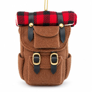 A brown felt backpack ornament or miniature bag with black faux-leather straps, gold-tone buckles, and a red-and-black buffalo plaid fabric top flap, shown on a white background.
