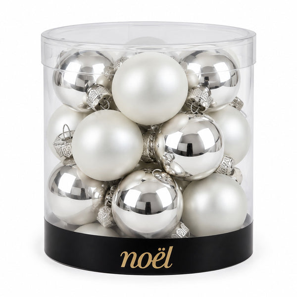 A set of silver and white Christmas tree ornaments inside a clear cylindrical container with a black base printed with the gold 'noël' brand name, on a white background.