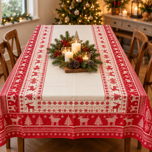 A festive Christmas table runner with a red and white Nordic reindeer pattern, styled on a dining table with candles and greenery in a warmly lit holiday dining room.