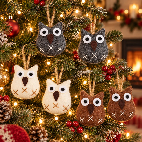 Six felt owl Christmas tree ornaments in gray, cream, and brown hang on a lit Christmas tree with warm fairy lights and holiday decorations.