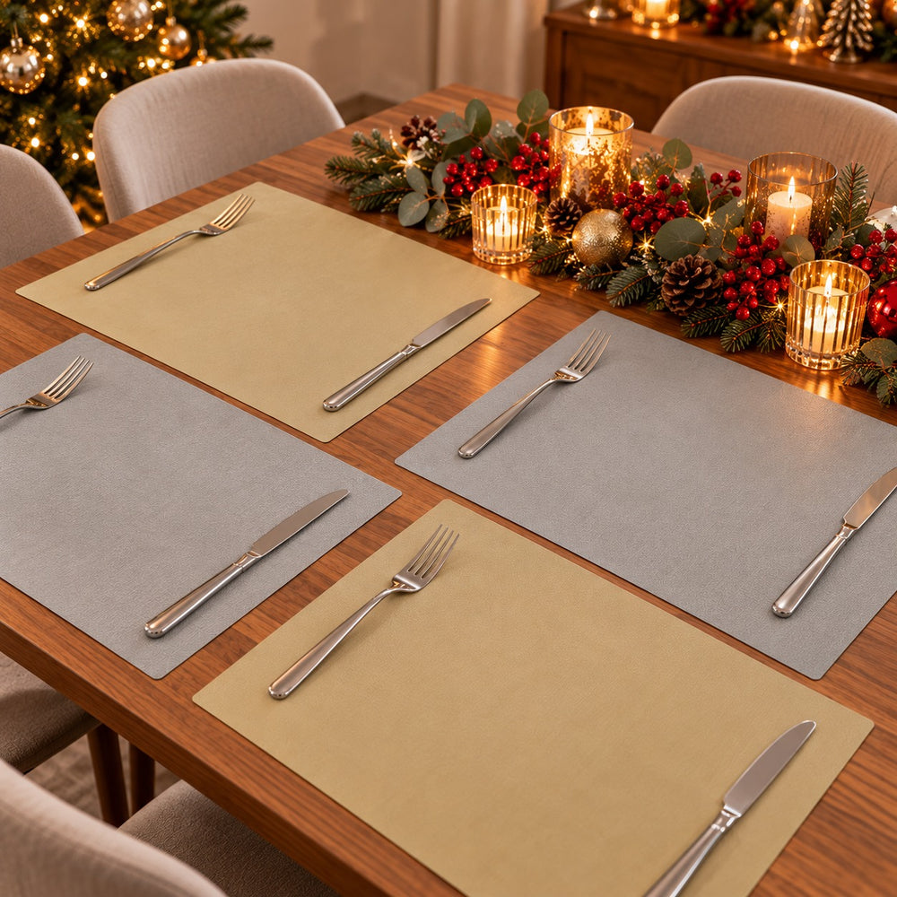 A beautifully set dining table for two during the holiday season, featuring beige placemats, white plates, silver cutlery, wine glasses, and napkins wrapped in a brown band, surrounded by festive greenery, red berries, and warm candlelight.