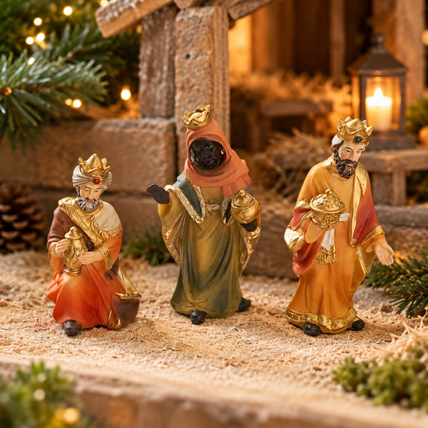 Three Christmas nativity figurines of the Three Wise Men in a stable scene with warm lighting, candles, and pine branches.