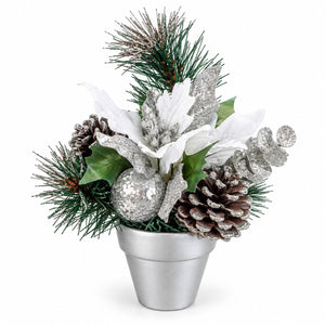 A festive artificial Christmas floral arrangement in a small silver pot, featuring white poinsettia-style flowers, green pine branches, brown pinecones, silver glitter accents, and holly leaves on a white background.