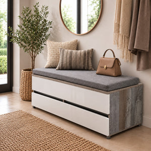 A modern storage bench with a gray upholstered cushion and white drawers, styled in a warm entryway with woven pillows, a handbag, a potted plant, and a round mirror.