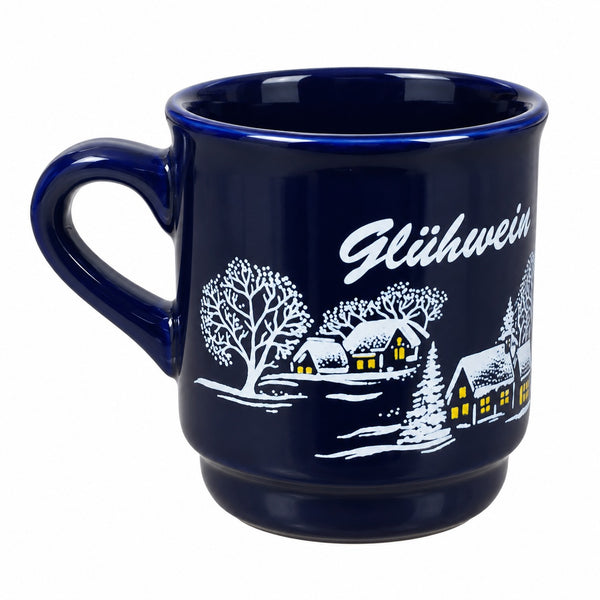 A dark blue ceramic mug featuring a white winter village illustration with glowing yellow windows and the word 'Glühwein' in white script.