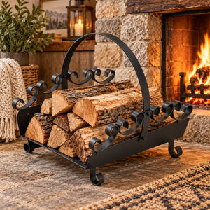 A black wrought-iron firewood log rack filled with cut logs, placed in front of a stone fireplace with a warm fire burning inside.