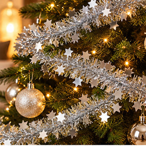 Silver tinsel garland with hanging star ornaments draped over a green Christmas tree with warm string lights and decorative baubles.