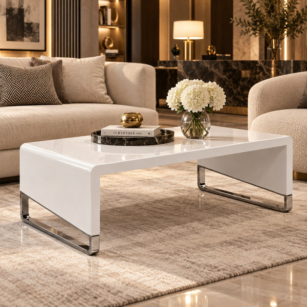 A modern low-profile coffee table with a glossy white rectangular top and chrome-finished metal legs, styled in a contemporary living room setting.