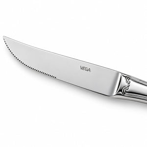 A close-up of a polished stainless steel dinner knife with a serrated edge, featuring the VEGA brand name engraved on the blade and an ornate handle, set against a clean white background.