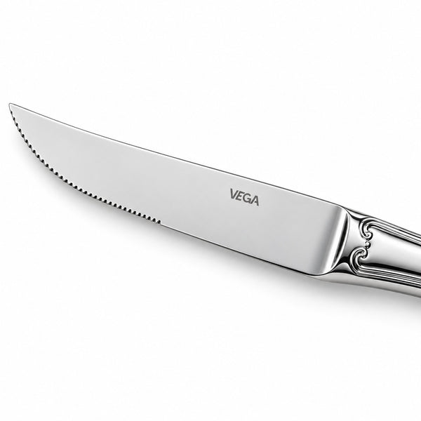 A close-up of a polished stainless steel dinner knife with a serrated edge, featuring the VEGA brand name engraved on the blade and an ornate handle, set against a clean white background.