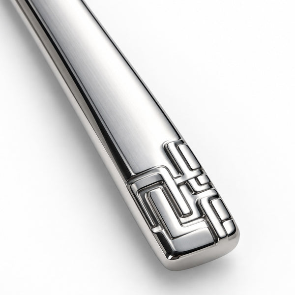 A close-up of a polished silver metal utensil handle, likely a spoon or spatula, featuring a geometric engraved pattern near the end, set against a clean white background.