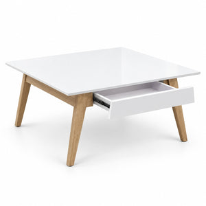 A modern square coffee table with a glossy white top and drawer front, supported by four angled light oak wood legs. One drawer is pulled open, showing a dark interior.