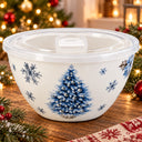 A white ceramic holiday bowl with a clear plastic lid, decorated with a blue Christmas tree and snowflakes, set on a wooden table with festive holiday decorations in the background.