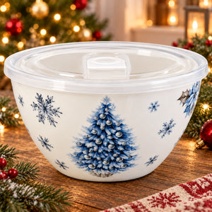 A white ceramic holiday bowl with a clear plastic lid, decorated with a blue Christmas tree and snowflakes, set on a wooden table with festive holiday decorations in the background.